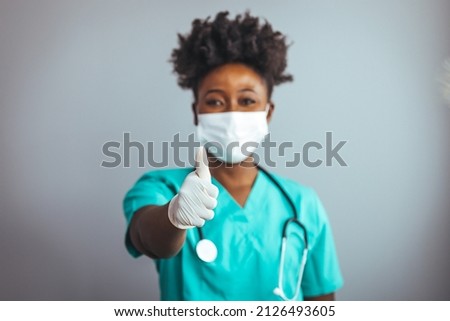 Friendly nurse with stethoscope isolated on grey. Smiling female healthcare professional looks at the camera while in hospital hallway. She is standing with her arms crossed.