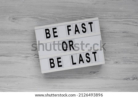 'Be Fast or Be Last' on a lightbox on a white wooden background, top view. Flat lay, overhead, from above. 