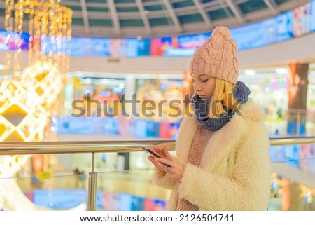 teenage girl in white jacket in shopping mall watch phone.