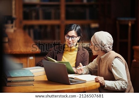 Warm toned portrait of two adult women studying together in classic college library, copy space