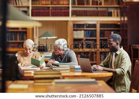 Side view portrait of young black man using laptop while studying college library with people in background