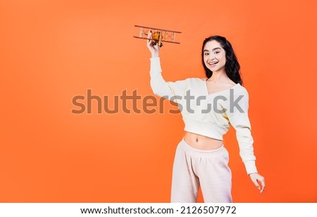 Smiling mixed race woman holding toy wooden airplane. Tourism, travel or airplane flight concept. Mockup background with copy space for travel agency advertisement.