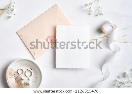 Elegant wedding stationery set. Flat lay wedding invitation card template, pastel pink envelope, silk ribbon, golden rings, flowers on marble desk.