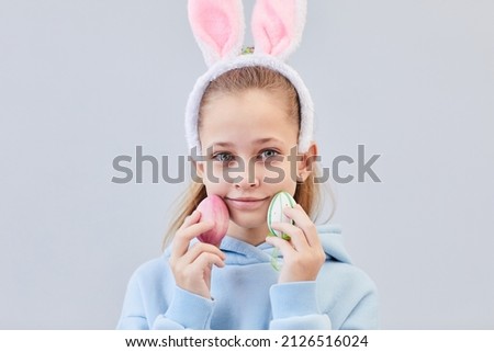 Front view portrait of cute teenage girl wearing bunny ears and holding Easter eggs against white background, copy space