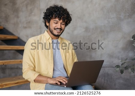 Smiling Indian man using laptop computer typing working freelance project from home. Handsome asian student studying, learning language, online education concept. Programmer sitting at workplace  Royalty-Free Stock Photo #2126525276