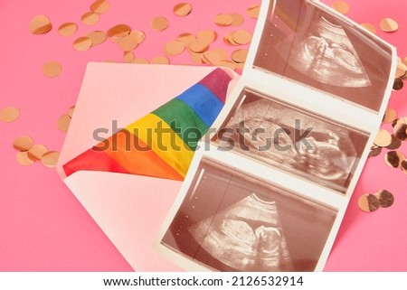 rainbow colors flag and pregnancy ultrasound scan in pink envelope, pregnancy and lgbt couple, pride concept, pink background with confetti, gender party