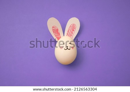 Food photo. White chicken egg with cute rabbit face and bunny ears on a purple background. Greeting card for religious holiday Happy Easter. Preparation for the celebration. Banner. Copyspace. Poster