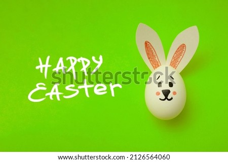 Food photo for Easter. Chicken egg with a cute rabbit face and rabbit ears on a green background. Greeting card for Easter holiday. Happy Easter text. Preparation for the celebration. Family holiday