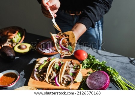 Mexican woman hands preparing tacos with carnitas pork and sauce in Mexico city