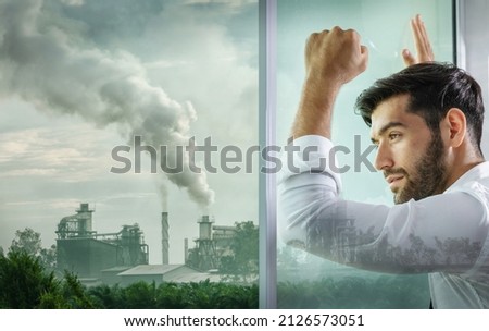 A businessman looks out of a window filled with industrial air pollution.