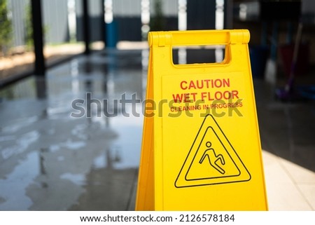 "Caution, Wet floor" with slip icon, a safety information sign which is placed in front of toilet during cleaning is in progress. Close-up and selective focus.