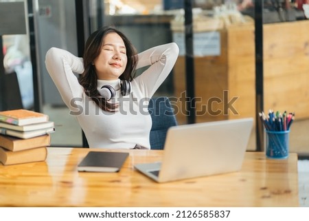 Happy calm asian girl student relaxing holding hands behind finished study work breathing fresh air sit at home office desk feel stress relief stretching doing exercise dreaming enjoy peace of mind