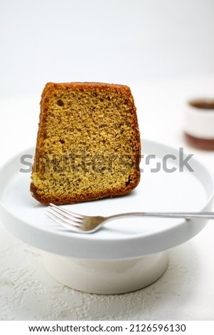 a slice banana sponge cake with a white plate and a glass of tea in a brigtmood, selective focus, blur background