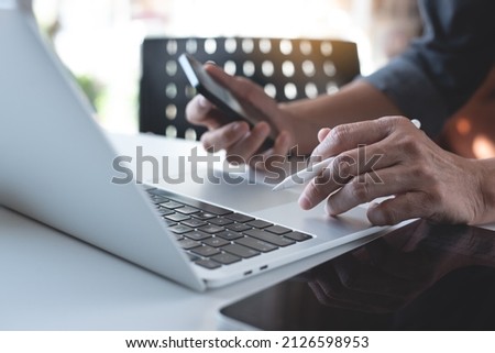 Close up of multi-tasking business man working on laptop computer, using mobile smart phone and digital tablet at home office. Male freelancer, graphic designer at work, telecommuting