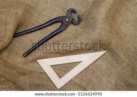 Pincers, triangular ruler and Rough Fabric Bagging on Dark Wooden Background. Cracked wooden surface with cracks and splinters. Selective focus.
