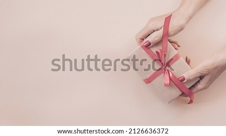 Woman hands holding gift decorated with red ribbon on pink background, copy space. Flat lay, hands and present box, top view. Valentine or love, spring holidays, Christmas and birthday concept.