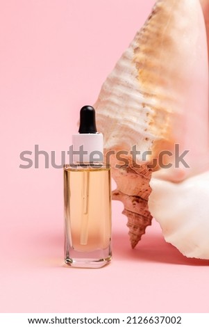 Close up of glass cosmetic bottle with dropper on a pink background near of strombus gigas sea shell. Vertical orientation. The concept of an advertising template for beauty products.