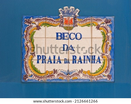 Beautiful street sign "Beco da praia da Rainha" in Portugal. Fragment of traditional Portuguese concrete signs with road name of colorful ceramic tiles. Background from painted Azulejo tiles. Royalty-Free Stock Photo #2126661266