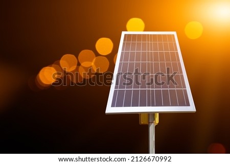 Mini solar cell panel edited with blurred bokeh street lamps at night background, concept for using energy from the sunlight with human life everywhere at night.