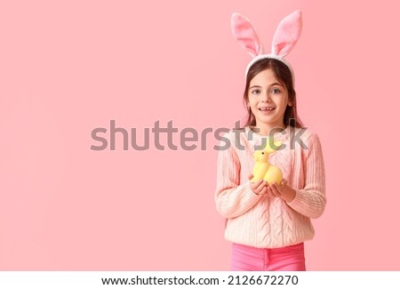 Cute little girl with bunny ears and toy rabbit on pink background. Easter celebration