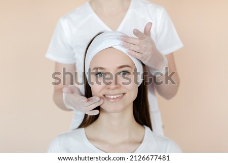A happy woman with a white bandage on her head is having a facial massage. Close-up of a woman's face and hands of a beautician. High quality photo