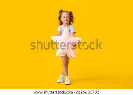 Adorable little girl with pillow in shape of star on yellow background