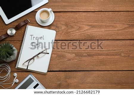 Notebook with phrase Travel Tips, cup of coffee and tablet on wooden table, flat lay. Space for text