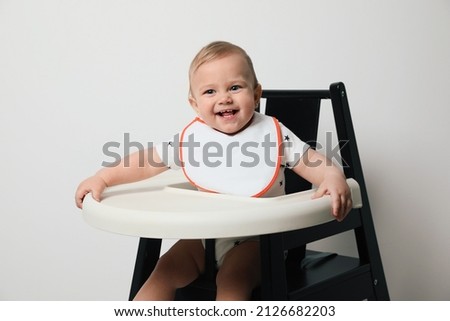 Cute little baby wearing bib in highchair on white background Royalty-Free Stock Photo #2126682203