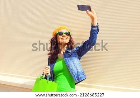 Portrait of happy smiling woman with shopping bags taking selfie by smartphone on city street