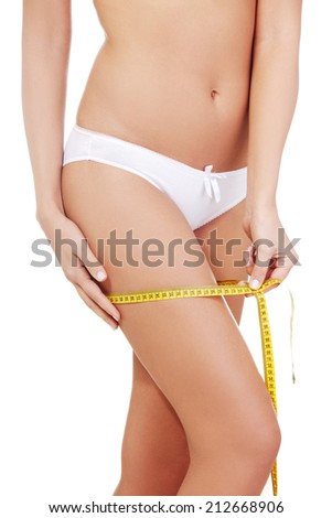 Closeup photo of a Caucasian woman's leg. She is measuring her thigh with a yellow metric tape measure after a diet