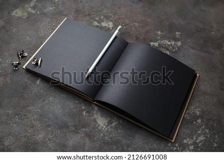 Blank black opened book and pencil on concrete background. Template for graphic designers portfolios.