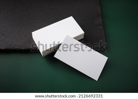 Blank white business cards and stone board on green table background. Copy space.