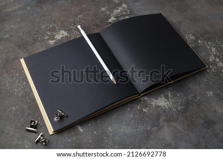 Photo of blank opened black brochure and pencil on concrete background. Template for graphic designers portfolios.