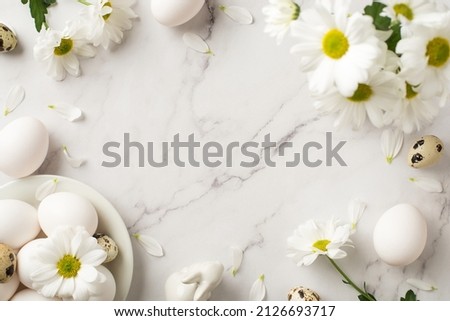 Top view photo of easter decorations bouquet of chrysanthemum flowers petals ceramic easter bunny and plate with eggs on isolated white marble texture background with empty space in the middle