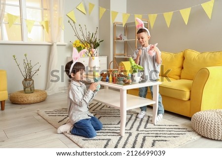 Cute little boys with bunny ears painting Easter eggs at home