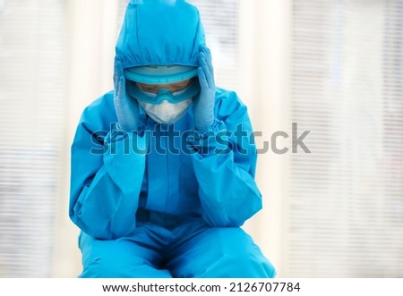 Tired female doctor in personal protective equipment PPE feeling depressed after difficult stressful shift during Covid-19 pandemic, sitting on floor in hospital. Overwhelmed health care workers