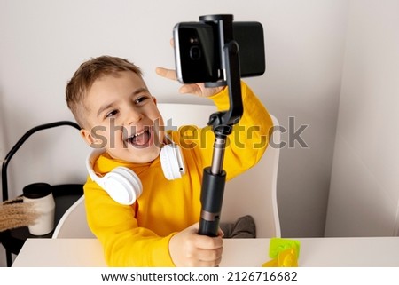 Adorable, cute, little boy blogger recording lifestyle blog, talking to camera of smartphone on tripod. Young influencer filming vlog for his channel. Child makes video for his followers online.