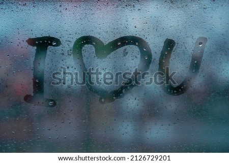 Abbreviated inscription I Love You on the wet fogged glass on a rainy day