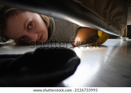 Woman cleaner looking under sofa for sock using flashlight Royalty-Free Stock Photo #2126733995