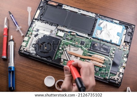Soldering iron in hand, disassembled laptop. Top view. Repair shop.A worker with tools. Computer equipment.Soldering iron.A digital device.The laptop is on the table.The Concept Of Electronic Devices. Royalty-Free Stock Photo #2126735102