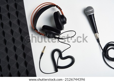 Microphone, headphones and heart shaped cable on on white background with acoustic foam panel on side