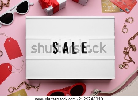 Lightbox with word Sale, credit cards and fashionable accessories on pink background, flat lay