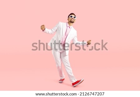 Happy funny guy in white suit dancing isolated on pastel pink background. Full body shot of cheerful goofy carefree man in modern suit, sneakers and glasses dancing and having fun in the studio Royalty-Free Stock Photo #2126747207