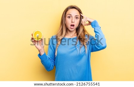 pretty woman looking surprised, realizing a new thought, idea or concept holding half orange