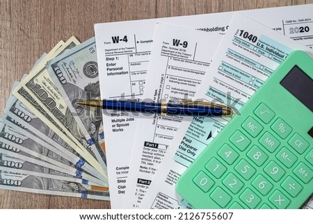 tax forms 1040 are blank to fill out and dollars are sloppily scattered on a wooden table. The concept of working time in the office