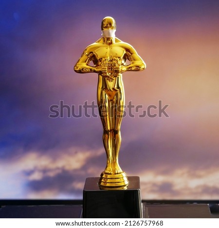 Hollywood Golden Oscar Academy award statue in medical mask on sky background. Success and victory concept. Oscar ceremony in coronavirus covid-19 time