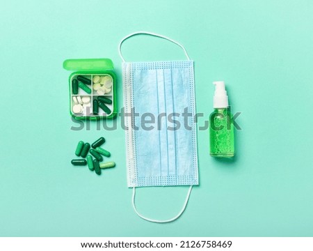 Medical mask, hand sanitizer and box with different pills on color background