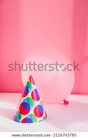 Pink inflatable balloon and a colorful festive hat on top for a birthday party.