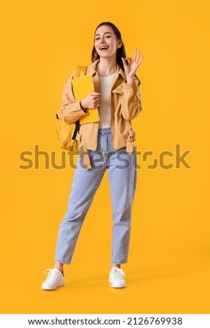 Portrait of beautiful female student showing OK gesture on color background Royalty-Free Stock Photo #2126769938