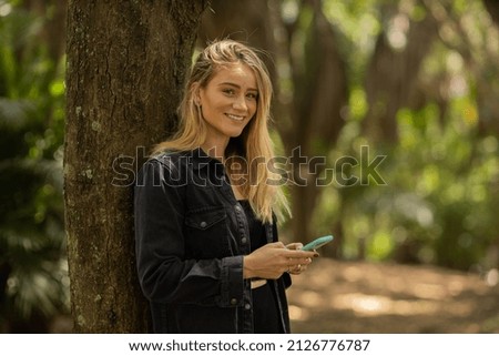 Young woman using a smartphone at day time with a green park in the background. High quality photo. Mobile phone, technology, urban concept. High quality photo